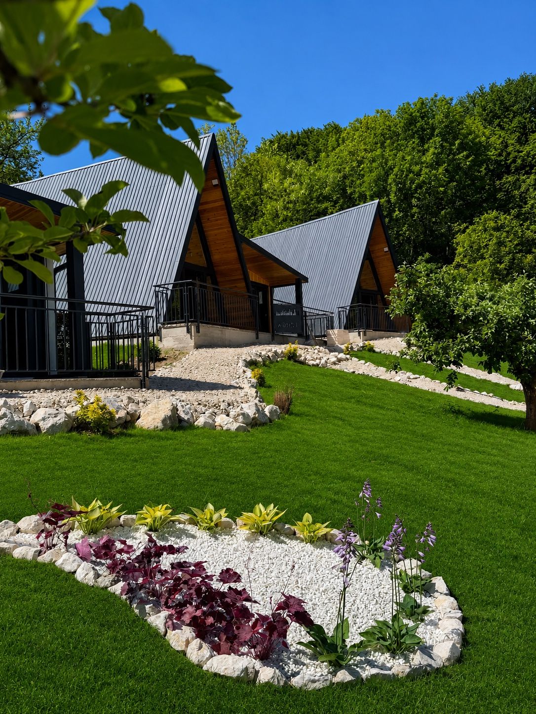 Două cabane A-frame negre în spatele unui strat de flori.