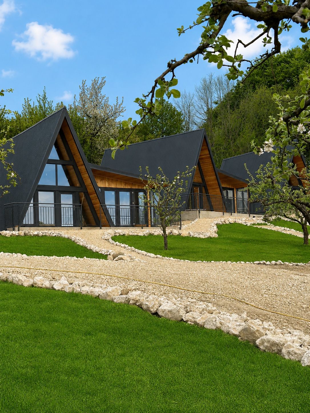 Trei cabane A-frame negre, așezate în șir pe un deal verde.